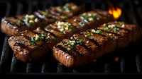 Juicy grilled beef steaks with garlic butter and fresh herbs cooking on flaming barbecue grill, close-up view showing grill marks and melting seasoning.