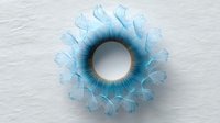 Delicate circular pattern in light blue tones with translucent petal-like elements radiating from center ring, creating ethereal mandala effect on white background.