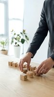 Businessman arranging wooden blocks with business icons on office desk. Strategic planning and organization concept for corporate development.