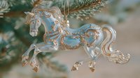 Elegant glass horse ornament with gold accents hanging on Christmas tree, showcasing delicate craftsmanship and festive holiday decoration.