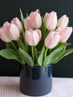Fresh pink tulips arranged in dark blue ceramic vase on white checkered tablecloth against black background for spring home decor and floral arrangements.