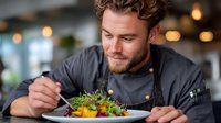 Professional chef garnishing gourmet dish with microgreens in modern restaurant kitchen. Culinary expert preparing fine dining meal with artistic presentation.
