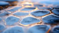 Frozen honeycomb pattern with golden sunlight creating luminous edges on ice crystals. Natural geometric shapes form abstract winter macro photography background.
