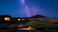 Modern eco lodge under starry night sky with Milky Way galaxy visible above desert landscape and illuminated pathway leading to luxury accommodation.