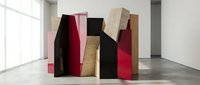 Modern abstract sculpture installation with geometric wooden blocks in red, black, pink and natural wood tones displayed in contemporary gallery space.