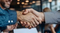 Close-up of diverse business professionals shaking hands in modern office setting, symbolizing partnership, trust and successful deal completion.
