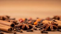Aromatic spices including cinnamon sticks, star anise, cloves and peppercorns scattered on warm wooden surface for culinary and cooking projects.