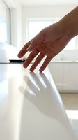 Hand of person with medium skin tone resting on white glossy surface in bright modern interior space, casting shadow, suitable for business, technology, wellness, and corporate design projects.