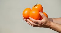 Hand holding three fresh ripe oranges against neutral background. Suitable for food, nutrition, healthy lifestyle, grocery, and wellness marketing materials.