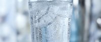 Clear sparkling water with ice cubes in glass against blurred background for refreshment and hydration concepts in restaurants and cafes.