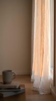 Sunlight filtering through sheer linen curtains in a minimalist room with wooden floor, ceramic mug and books, creating warm natural light for home decor and interior design projects.