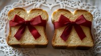 Golden brioche bread slices with burgundy ribbon bows on white lace doily, festive breakfast concept for holiday morning meals and special occasions.