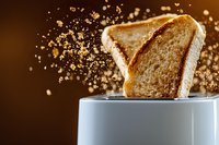 Golden toast popping up from white toaster with flying crumbs and motion blur against dark brown background, dramatic morning breakfast scene.