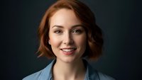 Professional young Caucasian woman with short red hair smiling confidently in denim jacket against dark background for business portraits.