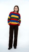 Young woman with long dark hair and fair complexion wearing a vibrant multicolored striped knit sweater in red, blue, yellow and green with black velvet trousers for casual fashion styling.