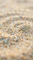 Close-up of colorful sand grains in various shades of cream, tan, blue and yellow. Shallow depth of field creates soft focus background. Use for beach, nature, texture, and environmental backgrounds.