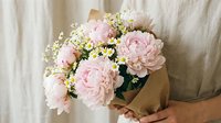 Pink peony bouquet with baby's breath wrapped in kraft paper held by woman, perfect for Mother's Day gifts, weddings, romantic occasions and floral arrangements.