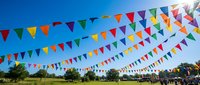 Colorful triangular bunting flags strung across blue sky at outdoor festival or celebration event. Party decoration banners create festive atmosphere for community gathering.