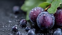 Fresh purple plums with water drops on dark background, macro shot showing juicy ripe fruit texture and natural moisture. Green leaves add organic appeal.