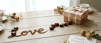 Rustic wooden table with Love written in cocoa powder, heart chocolates, floral gift box, and Happy Valentine card for romantic holiday celebration.