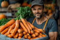 Caucasian male farmer in apron displaying fresh organic carrots with green tops at local market stall, authentic farm-to-table produce shopping experience.