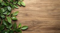 Fresh green leaves and branches arranged on rustic wooden background with natural grain texture, creating corner border composition for organic design.
