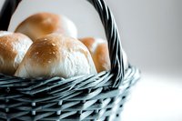 Fresh homemade dinner rolls in rustic blue woven basket against light background, close-up view showing soft texture and golden brown crust.