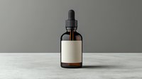 Dark amber glass dropper bottle with blank white label on textured marble surface against neutral gray wall background, minimalist product photography setup.