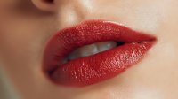 Close-up of woman's lips with glossy red lipstick showing natural skin texture and partial smile for beauty and cosmetics advertising.