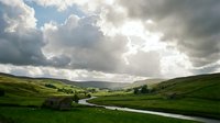 Scenic rural valley landscape with winding river, rolling green hills, and dramatic cloudy sky, suitable for nature backgrounds and environmental design projects.