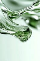 Flowing liquid with green spherical particles suspended in transparent fluid creates dynamic abstract composition with soft curves and light reflections.