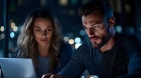 Business professionals working late on laptop computer in modern office with city lights background at night.