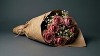 Elegant bouquet of dusty pink roses with baby's breath wrapped in brown kraft paper against dark background for romantic occasions and floral arrangements.