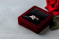Heart-shaped diamond engagement ring in red velvet box with rose, romantic proposal setting on light background, selective focus on jewelry.