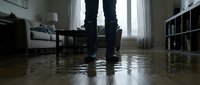 Person standing in flooded home interior with water damage on hardwood floors during emergency situation requiring cleanup and restoration services.