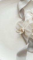 Elegant white orchid flower with flowing silk ribbon on neutral beige background for wedding invitations and luxury branding projects.