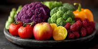 Fresh colorful fruits and vegetables on rustic plate, including purple cauliflower, broccoli, berries, citrus, apple, tomato and bell pepper.