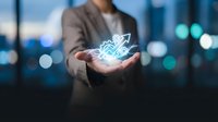 Businesswoman holding glowing digital growth chart with upward arrow in palm against blurred city skyline at dusk, representing financial success and data analytics.
