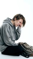 Young Caucasian man in gray hoodie sitting with head in hands showing stress, depression or mental health struggles isolated on white background.