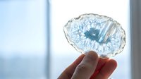 Blue agate slice with natural crystalline formations held against bright window light showcasing translucent mineral patterns and geological beauty.