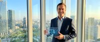 Professional businessman in dark suit holding blue award trophy in modern office with city skyline view through floor-to-ceiling windows during daytime.