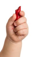 Child's hand holding red crayon isolated on white background, showing creative art supplies for educational and learning concepts.