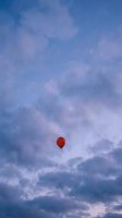 Single red balloon floating in dramatic blue and purple cloudy sky during twilight hour creating dreamy atmospheric scene for romantic concepts.