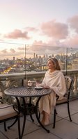 Elegant blonde woman enjoying coffee on luxury rooftop terrace at sunset with city skyline view for lifestyle and hospitality concepts.