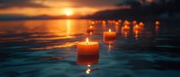 Glowing candles floating on calm water surface at sunset, creating peaceful atmosphere with golden light reflections and bokeh effect in panoramic view.