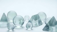 Transparent glass geometric shapes and spheres arranged on a white surface, showcasing crystal-clear pyramids, diamonds, and orbs in soft light.