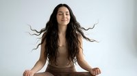 Young woman with long flowing hair meditating in peaceful pose against white background. Wellness lifestyle concept for relaxation and mindfulness practice.