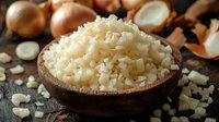Fresh chopped onion pieces in wooden bowl on rustic dark background with raw onions and scattered pieces, macro food photography for cooking blogs.