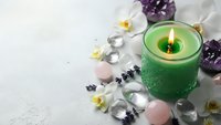 Green aromatherapy candle burning with healing crystals, white orchids and lavender sprigs on marble surface for spa wellness and meditation.