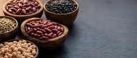 Assorted legumes and beans in wooden bowls on dark slate surface, including red kidney beans, black beans, chickpeas, and lentils for cooking and nutrition.